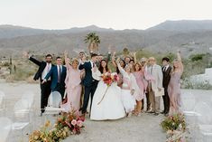 a group of people standing next to each other on top of a dirt field with palm trees in the background