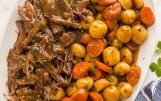 a white plate topped with meat, potatoes and carrots next to a blue napkin