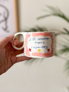 a hand holding a coffee mug with writing on it that says just another manic rummage