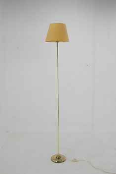 a floor lamp with a yellow shade on the base and a white wall behind it