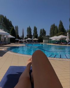 a person laying down in front of a swimming pool with umbrellas and lounge chairs