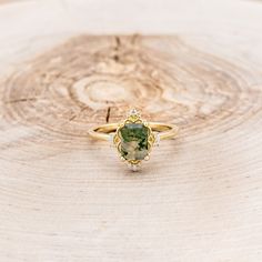 a gold ring with a green stone on it sitting on top of a tree stump