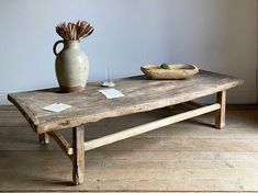 an old wooden table with a vase on it and two empty glasses sitting on top