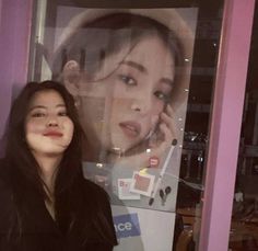 a woman standing in front of a window talking on a cell phone and smiling at the camera