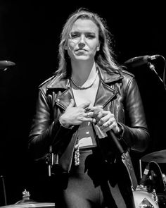 a woman in tights and a leather jacket standing next to a microphone on stage