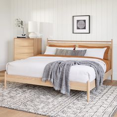 a bed with white sheets and pillows in a bedroom next to a rug on the floor