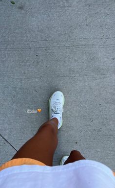 a person standing on the sidewalk with their feet up in front of them, wearing white sneakers