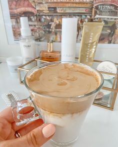 a hand holding a cup of coffee with whipped cream on top and other items in the background