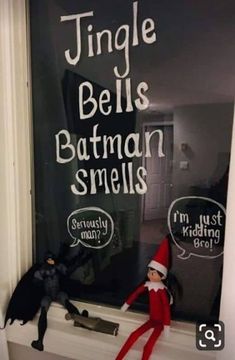 an elf is sitting on the window sill next to two toy bats and a batman