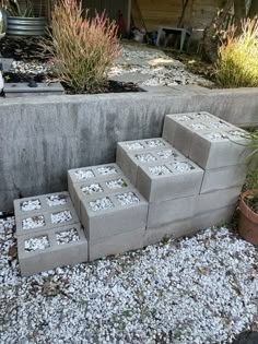 four cinder blocks are stacked on top of each other in front of some plants and gravel