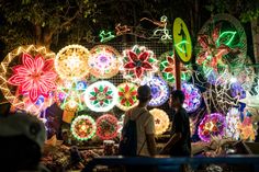 people are standing in front of colorful lights on display at an outdoor market area,