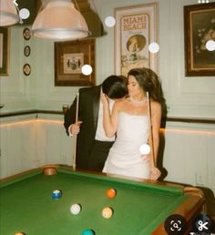 a bride and groom standing next to a pool table with billiards on it