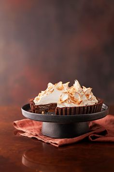 a chocolate pie with whipped cream on top sitting on a cake plate next to a red napkin