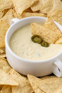 a white bowl filled with dip surrounded by tortilla chips and jalapenos