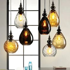 five glass hanging lights in front of a window with a vase on the table next to it