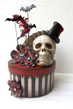 a skull wearing a top hat with flowers and bats on it's head sitting in a striped box