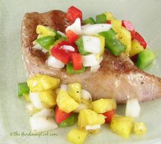 a white plate topped with meat covered in fruit and vegtables on top of it