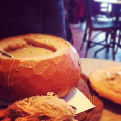 a bowl of soup sitting on top of a wooden cutting board next to some bread