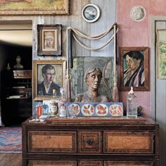 an old dresser with paintings and pictures on the wall