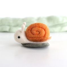 a small felt snail sitting on top of a white table next to a green blanket