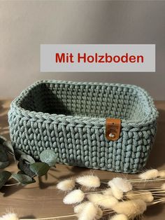 a knitted basket sitting on top of a wooden table next to some dried plants