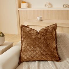 a brown pillow sitting on top of a white couch next to a vase with flowers