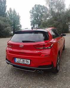 the rear end of a red car parked on top of a gravel road next to trees