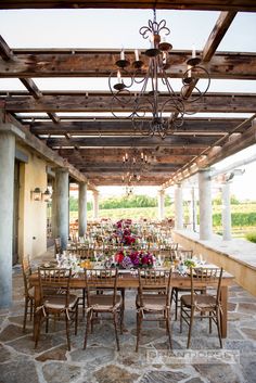 an outdoor dining area with tables, chairs and chandelier in front of it