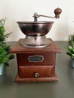 an old fashioned coffee grinder sitting on top of a table next to potted plants