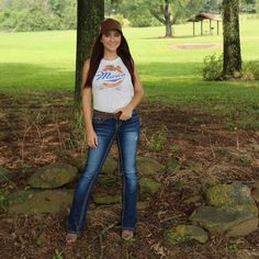 a woman standing in the woods wearing jeans and a t - shirt with an orange fish on it