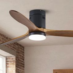 a black ceiling fan with wooden blades and a light on it's side next to a brick wall