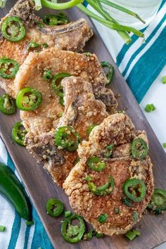 pork chops with green peppers and onions on a wooden cutting board next to sliced jalapenos