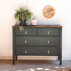 a green dresser with a potted plant on top and a wooden sign above it