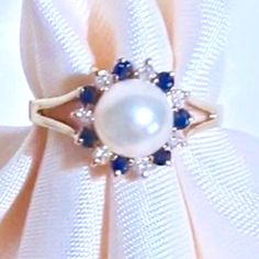 a close up of a ring with pearls and blue sapphires on white satin fabric