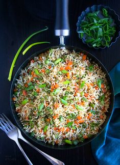 a pan filled with rice, carrots and green onions on top of a table