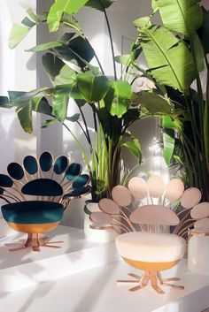 three colorful chairs sitting on top of a white table next to green plants and potted palm trees