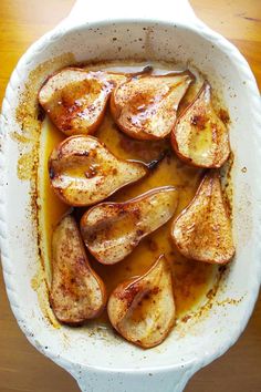 baked apples are in a white dish on a wooden table