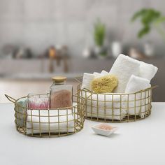 two metal baskets with towels and soaps in them on a white countertop next to a bowl