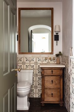 a white toilet sitting next to a wooden cabinet in a bathroom under a large mirror