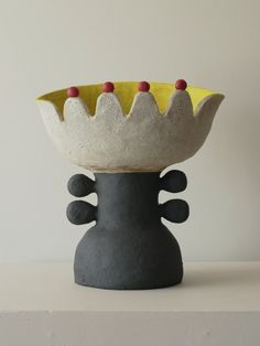 a ceramic bowl sitting on top of a white table next to a black and yellow vase