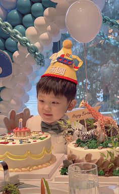 a young boy wearing a birthday hat sitting in front of a cake