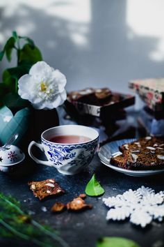 there is a cup of tea and some cookies on the table with flowers in the background