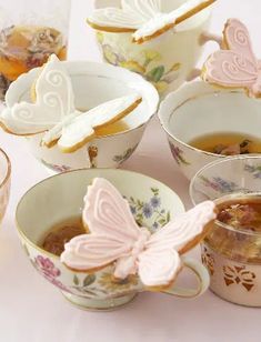 teacups with butterfly cookies in them sitting on a table next to cups and glasses