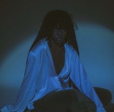 a woman with long hair sitting on the floor in a blue lit room and looking at the camera