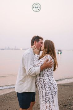 a man and woman kissing on the beach by the water at sunset with their arms around each other