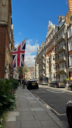 the british flag is flying high in the sky over an urban street with parked cars and tall buildings