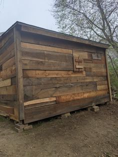 a small wooden building sitting on top of a dirt field next to a green tree