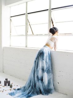 a woman leaning against a wall with her back turned to the camera, wearing a blue and white dress