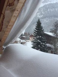 snow is covering the roof of a house in front of a snowy mountain and trees