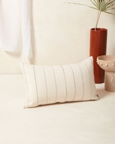 a white pillow sitting on top of a table next to a vase with a plant